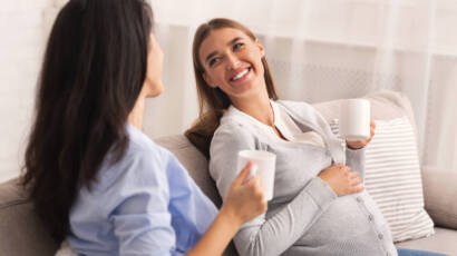 Pregnant Girl Talking With Friend Having Tea At Home